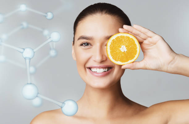 Happy young woman covering eye with orange half Happy young beautiful woman covering eye with orange half over grey background, molecular model, modern beauty industry concept oranges with faces stock pictures, royalty-free photos & images
