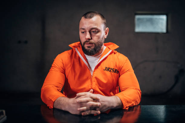 istock Prisoner in orange jumpsuit sitting alone in interrogation room 1198229767