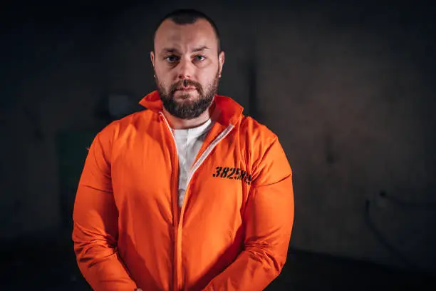One man, prisoner in orange jumpsuit standing alone in interrogation room.