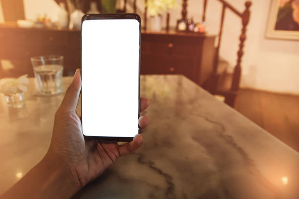 istock Hand holding mobile phone, blank white screen cell phone on marble table at coffee shop. Mockup image. 1198231209