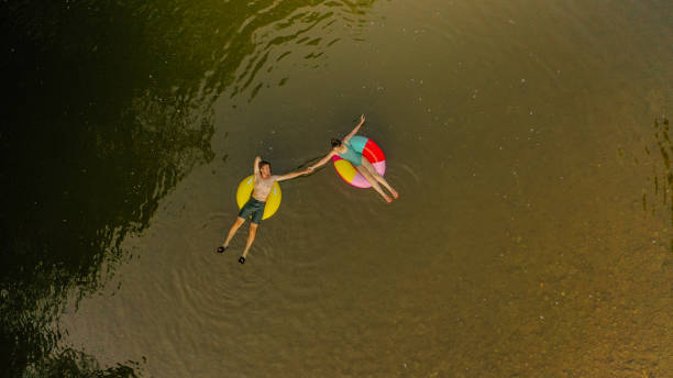 Young couple on inflatable rings in the river Photo of a young couple on inflatable rings in the river inner tube stock pictures, royalty-free photos & images