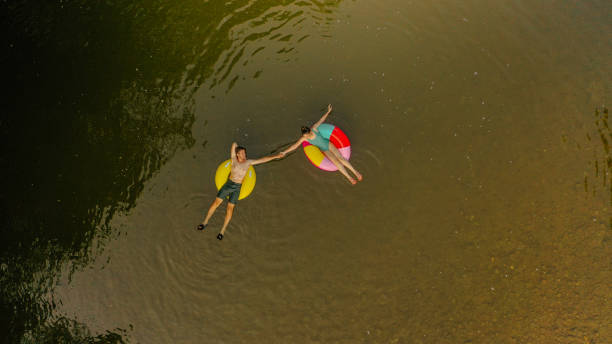 молодая пара на надувных кольцах в реке - inner tube swimming lake water стоковые фото и изображения