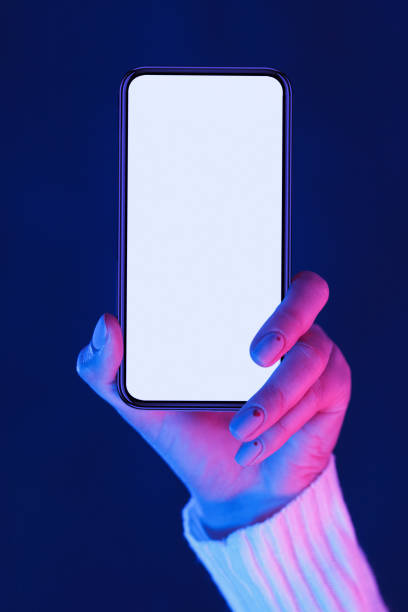 Female hand holding smartphone with blank screen in neon lights Female hand demonstrating modern smartphone with blank screen in neon blue and pink lights, vertical shot for mockup, free space, crop mobile phone lights up stock pictures, royalty-free photos & images