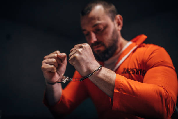 istock Prisoner in orange jumpsuit sitting alone in interrogation room 1198232496