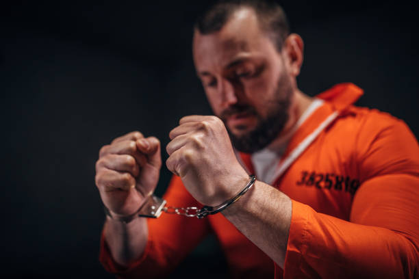 istock Prisoner in orange jumpsuit sitting alone in interrogation room 1198232515