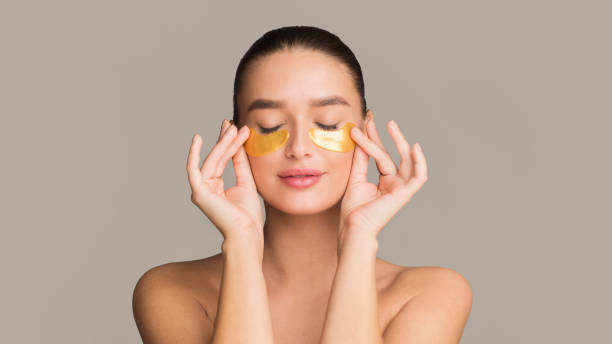 Young woman applying golden collagen patches under eyes Young woman applying golden collagen patches under eyes, taking care of delicate skin around eyes one eyed stock pictures, royalty-free photos & images