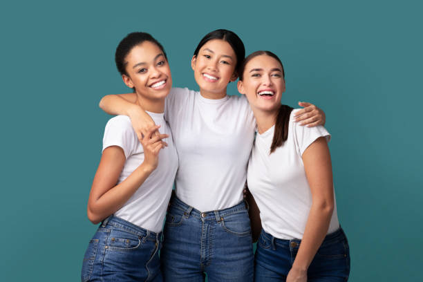 Three Happy Women Hugging Standing Over Turquoise Background, Studio Shot Girls Friendship. Three Happy Multiracial Women Hugging Smiling At Camera Standing Over Turquoise Background. Studio Shot japanese girlfriends stock pictures, royalty-free photos & images