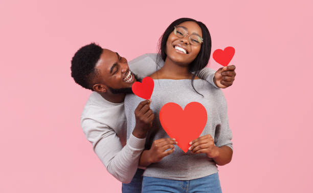 Afro couple in love holding red valentines cards St. Valentines day concept. Black couple in love holding red valentines cards and embracing, pink studio background boyfriend stock pictures, royalty-free photos & images