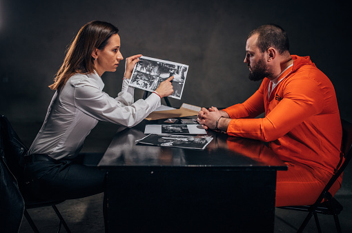 Woman detective interrogating a man prisoner in dark investigation room.