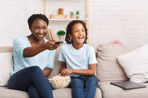 donna e ragazza afroamericana che guardano la tv con uno spuntino - movie time foto e immagini stock