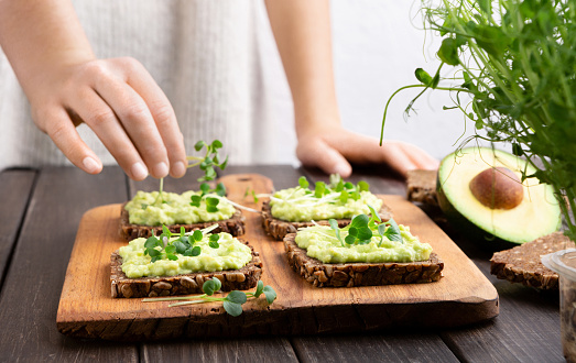 Food trends. Girl preparing wholegrain sandwiches with avocado spread and microgreen at kitchen, free space