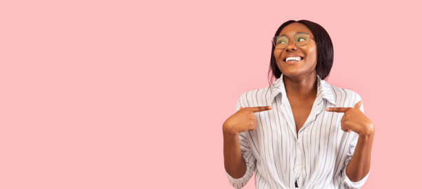 afro mujer señalando los dedos a sí misma sobre el fondo rosa, panorama - alardear fotografías e imágenes de stock