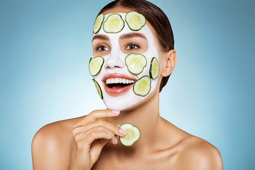 Happy young girl with facial mask and slices of cucumber on her face
