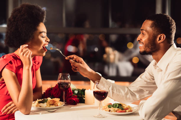 레스토랑에서 기념일을 축하하는 여자 친구를 먹이는 아프리카 계 미국인 남자 - anniversary couple rose black 뉴스 사진 이미지