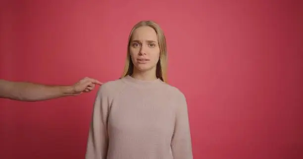 Someone hands gives virtual reality glasses into frame to blonde girl at pink wall.