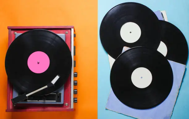 Retro style vinyl record player and vinyl records with covers on a colored paper background. Pop culture, Top view"n "n