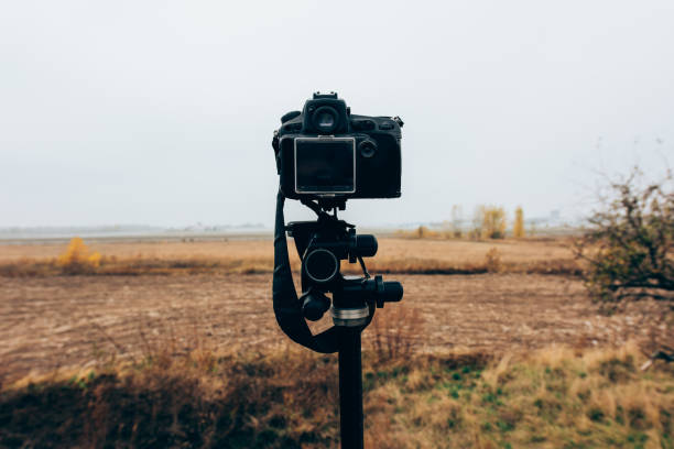 istock Selective focus of digital camera on tripod in grassy field 1198247103