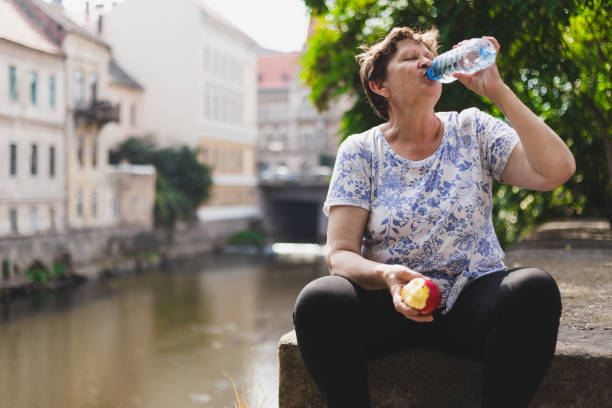 istock Exhausted granny holding a fruit in one hand while drinking from water bottle with the other 1198247513