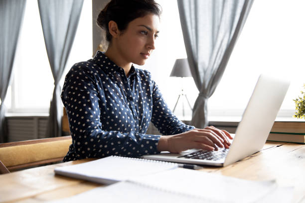 istock Serious indian woman student professional using laptop sit at desk 1198252553