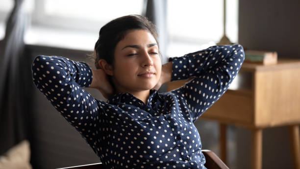 Calm indian lady rest at home office hands behind head Calm relaxed indian lady rest at home office sit on chair with eyes shut hold hands behind head, ethnic woman relax after work feel peace of mind dream think do exercises for neck back muscles relief meditation room office stock pictures, royalty-free photos & images