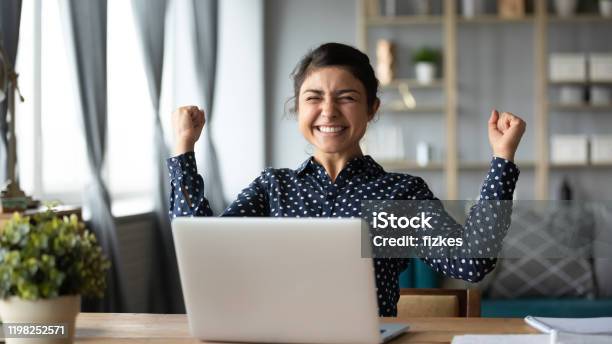 Photo libre de droit de La Jeune Fille Indienne Euphorique Célèbrent Le Triomphe De Victoire En Ligne Avec Lordinateur Portatif banque d'images et plus d'images libres de droit de Bonheur