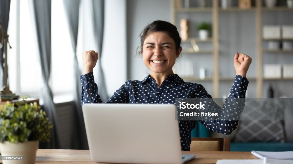 Euphoric young indian girl celebrate online victory triumph with laptop Euphoric young indian girl student winner celebrate victory triumph sit at home desk with laptop computer win online fortune feel excited get new job opportunity good exam result great news concept Happiness Stock Photo