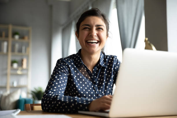 chica india alegre riendo sentarse con el ordenador portátil en la mesa - home worker fotografías e imágenes de stock