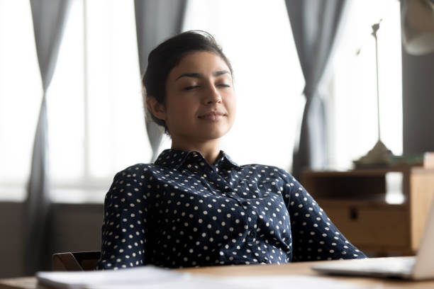 Relaxed indian young woman rest sit at desk eyes closed Relaxed indian young business woman meditate sit at work with laptop at desk with eyes closed, healthy lady take break to rest at home office breath fresh air feel stress relief peace of mind concept meditation room office stock pictures, royalty-free photos & images