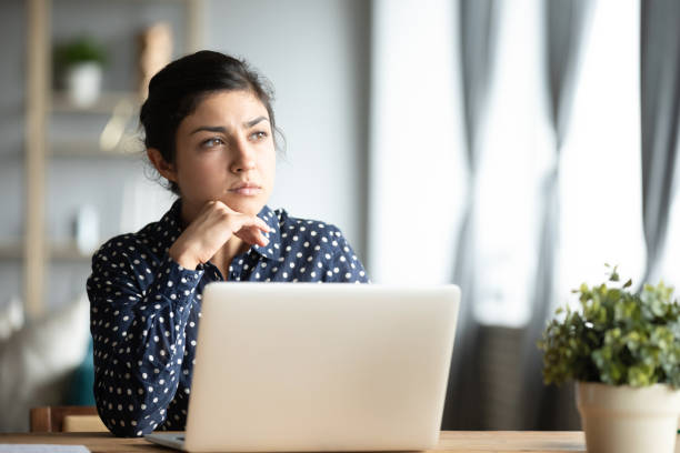 Serious thoughtful indian sit with laptop thinking of inspiration ideas Serious thoughtful pensive young indian ethnic woman student sit at home office desk with laptop thinking of inspiration solution lost in thoughts dreaming looking away search creative ideas concept introspection stock pictures, royalty-free photos & images