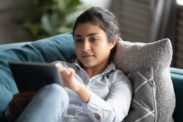 istock Indian woman resting at home on couch using digital tablet 1198252610