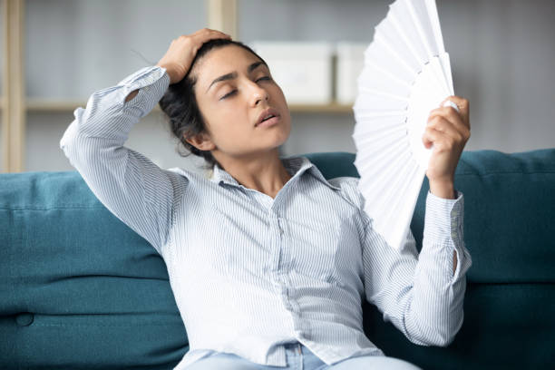 istock Tired indian woman using fan sit on couch at home 1198252621