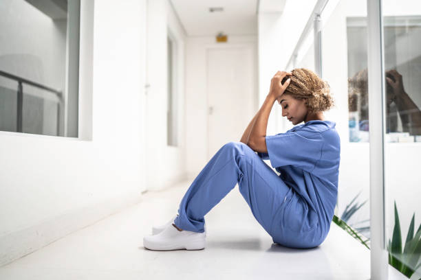Female nurse sitting on the floor and looking distraught Female nurse sitting on the floor and looking distraught oops stock pictures, royalty-free photos & images