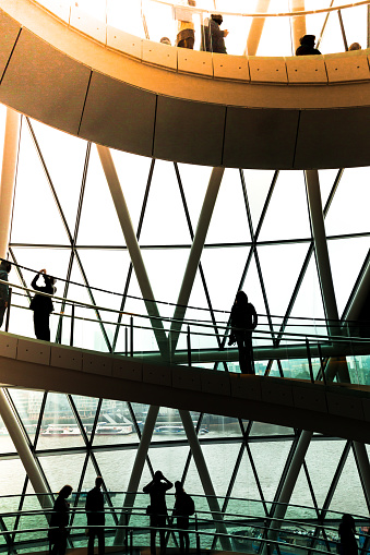 Color image depicting ultra modern contemporary interior architecture in City Hall (a public building in London that is open to the public) in London, UK. Crowds of people in silhouette and unrecognizable are walking down the modern spiral staircase. In the background we can see some of the skyscrapers that dominate the skyline of London. Lots of room for copy space.