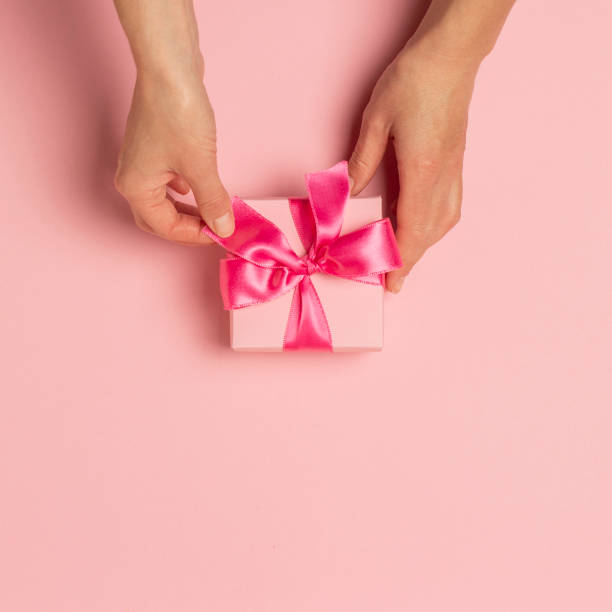 istock Female hands hold, take, receive a gift on a pink background. Wedding concept, Valentine's Day, a gift for a loved one. Flat lay, top view 1198260559