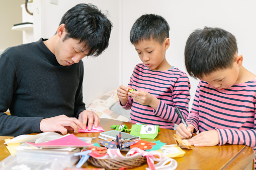A father with his sons is making art and craft from paper at home.