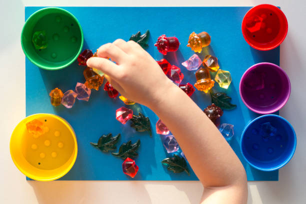 Child hand separating by color multicolored toy stones scattered on the blue surface into colorful cups