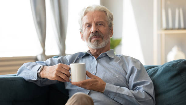 istock Elderly man sitting on couch holding cup looking at camera 1198265956