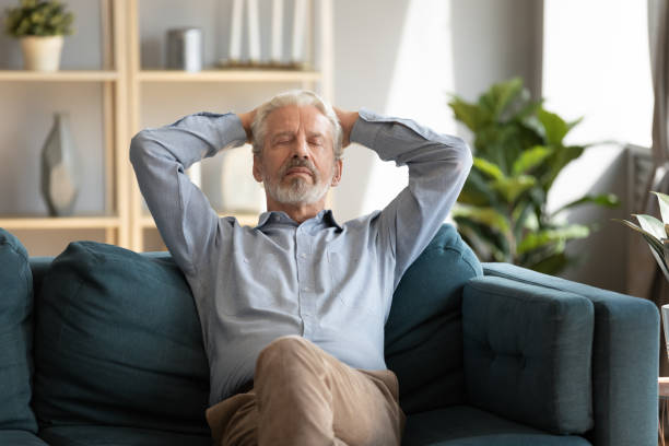 Mature man falls asleep leaned on couch in living room Hoary mature man falls asleep leaned on couch in living room, grandfather put hands behind head closed eyes looking tranquil resting feeling serenity, no stress, fresh air, pleasant solitude concept sleeping grandpa stock pictures, royalty-free photos & images