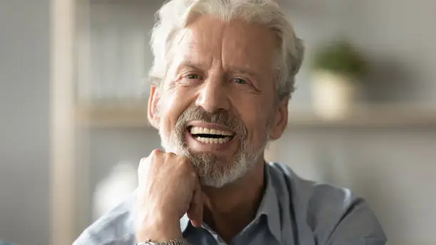 Close up portrait handsome face of 60s elderly man having candid wide toothy smile put fist under chin looking at camera concept of healthy person enjoy retired life, dentures services for old people