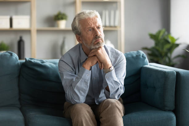 istock Pensive old 50s man seated on couch feels lonely 1198265967