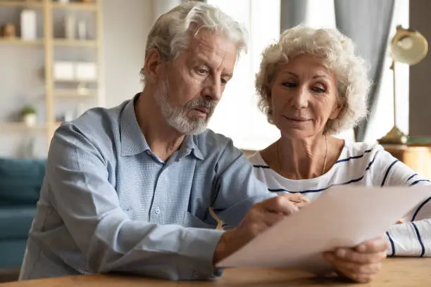 Photo of Mature couple read medical insurance terms seated at table indoors