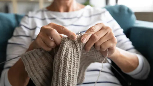 Close up view grandmother hands holding needles make repetitive motion knitting sitting on couch creating something with her arms. Hand knitting improve brain function, older generation hobby concept