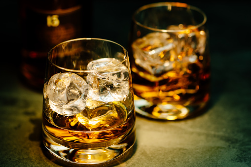 Two glasses of whiskey with ice, in a dark background.