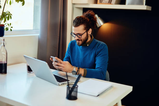 istock Smiling caucasian hipster sitting in his office and using smart phone for responding an e-mail. 1198267788