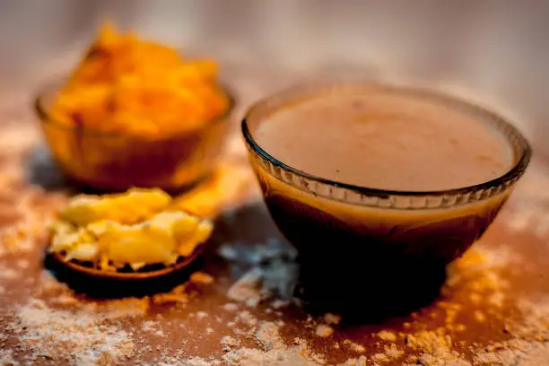 Photo of Close up of Indian Gujarati popular dish Atte ka sheera or Halwa-Karah parshad in a glass bowl on a brown surface with some spread wheat flour, jaggery and ghee or clarified butter.