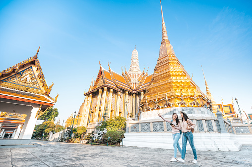 Tourist Asian women friends walking and enjoy sightseeing while travel in temple of the emerald buddha, Wat Phra Kaew, popular tourist place in Bangkok, Thailand