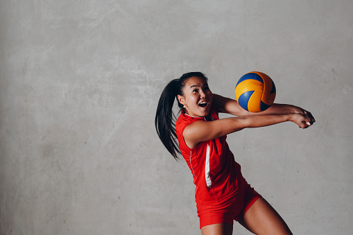 Joven sonriente asiática mujer jugadora de voleibol en uniforme rojo con pelota photo