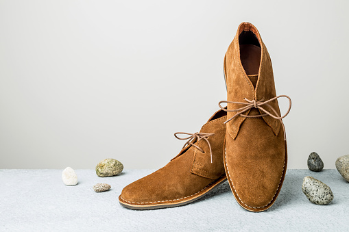 Fashion - men's camel suede desert shoes (boots) on grey background with stones around. Footwear - layout with free copy (text) space.