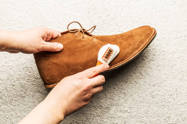 Suede desert shoe brush cleaning - footwear maintenance Hands cleaning men's camel suede desert shoe (boot) with a brush. Footwear maintenance captured from above (top view). Grey concrete background. camel colored photos stock pictures, royalty-free photos & images
