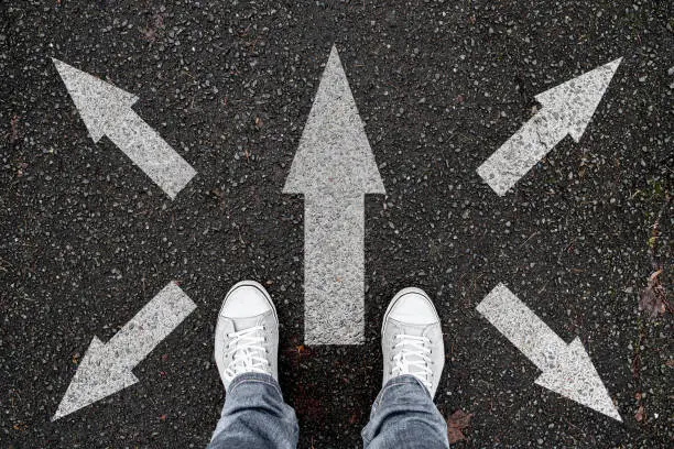 Photo of person standing on road with arrow markings pointing in different directions